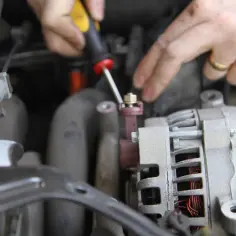 Mechanik dokręca śrubę przy alternatorze. Czas pracy: ile trwa wymiana alternatora w samochodzie?