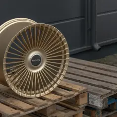 Złota felga aluminiowa z wieloma cienkimi ramionami, leżąca na drewnianych paletach.