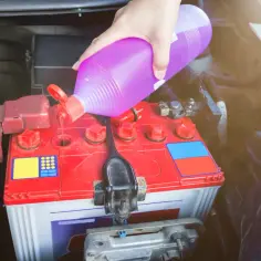 Ręka wlewa płyn do akumulatora samochodowego. To może być elektrolit do akumulatora AGM, który wymaga uzupełnienia.