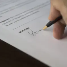 Dłoń podpisuje dokument. Co oznacza cr? To moment finalizacji umowy, ważny krok.
