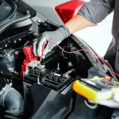 Mechanik sprawdza, jak sprawdzić alternator miernikiem, podłączając sondy do akumulatora samochodowego.