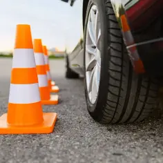 Pomarańczowe pachołki ustawione w rzędzie, obok samochodu, symbolizują wyzwania i testy na prawo jazdy.