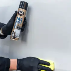 Rękawiczki ochronne i spray K2 Tar Remover pomagają usunąć naklejkę z samochodu. Żółta ściereczka poleruje powierzchnię.