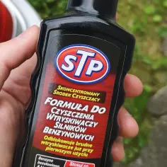 Dłoń trzyma butelkę STP z płynem do czyszczenia wtryskiwaczy. Skoncentrowana formuła odblokowuje brudne wtryskiwacze.