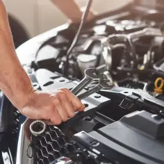 Mechanik naprawia silnik, trzymając klucze. Widać elementy układu paliwowego, w tym potencjalny zawór regulacji ciśnienia paliwa.