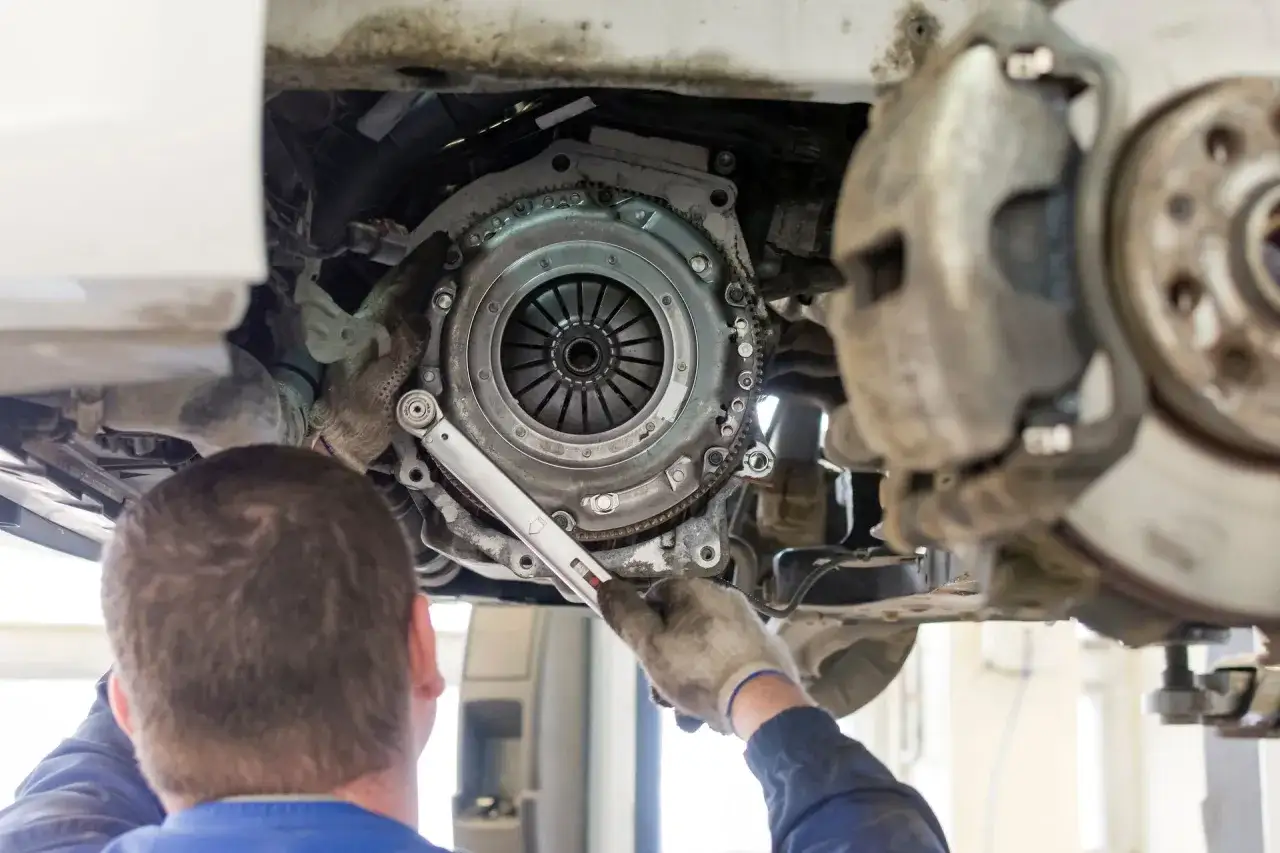 Mechanik dokręca śruby docisku, pokazując, jak zamontować tarczę sprzęgła. Widoczny jest też hamulec.