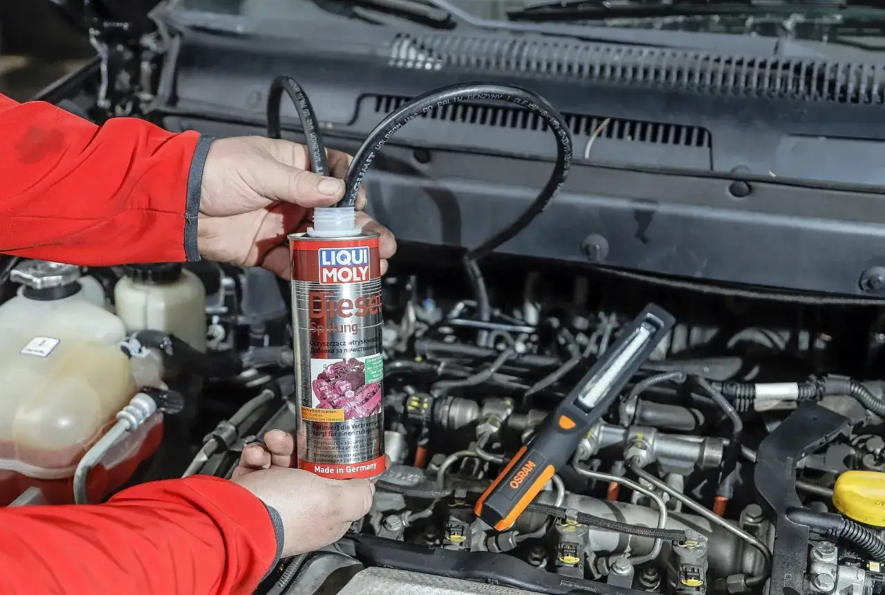 Mechanik używa preparatu do czyszczenia wtrysków diesel. Widać silnik i narzędzia.